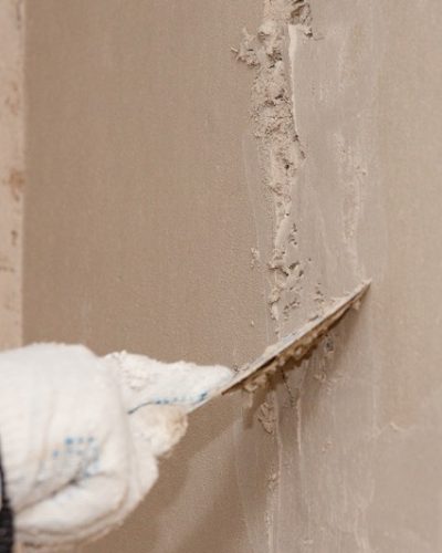 Hand with a spatula in the process of leveling the raw plaster.